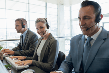 Three people with headsets on behind a desk.