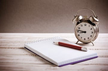 A clock on a table next to a notepad, time management for property management virtual assistants concept