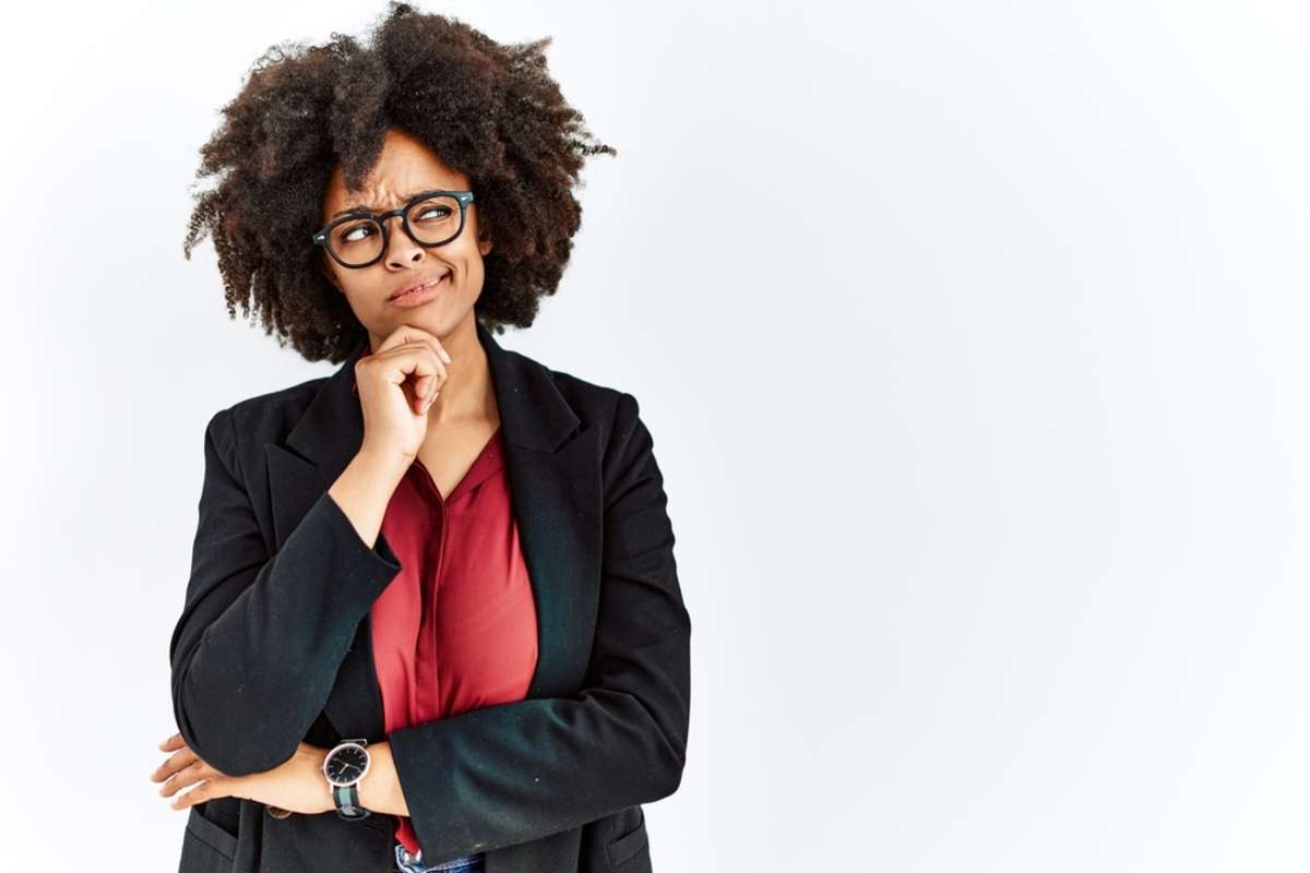 A woman with afro hair wearing a business jacket and glasses thinking, good virtual property management concept.