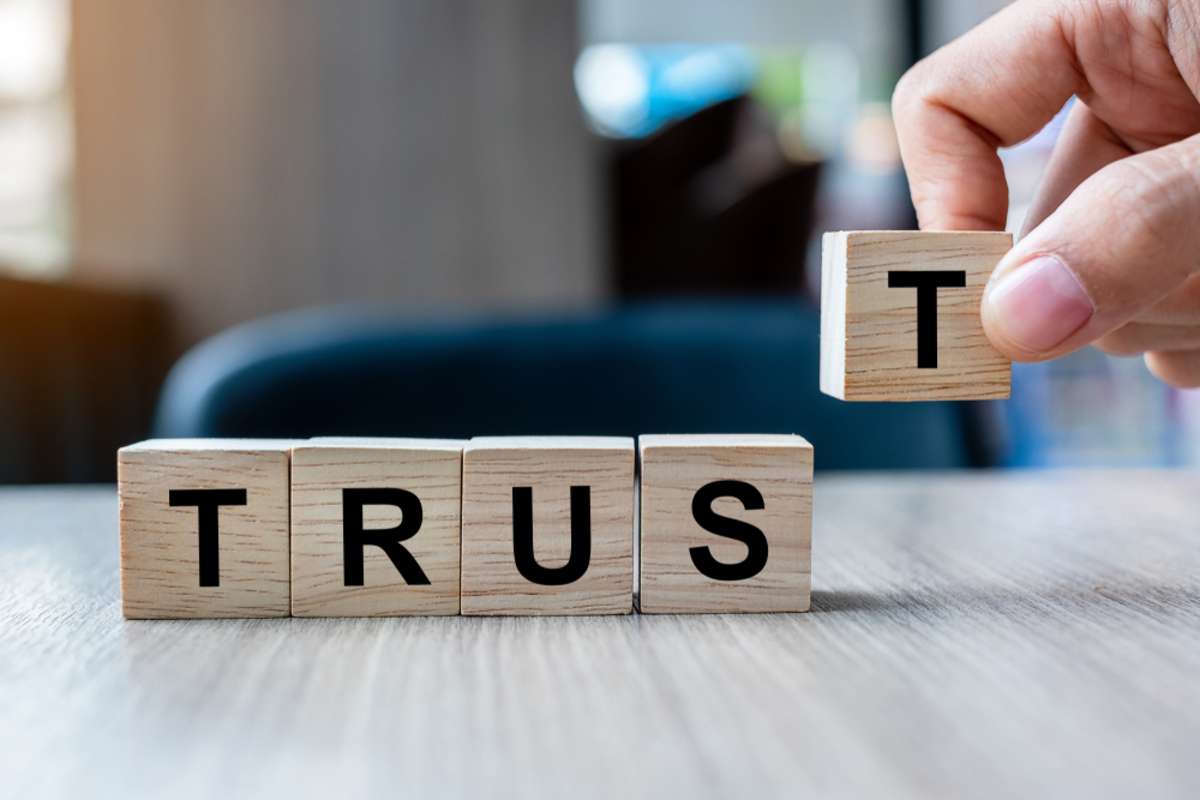 Businessman hand holding wooden cube block with TRUST business word on table background