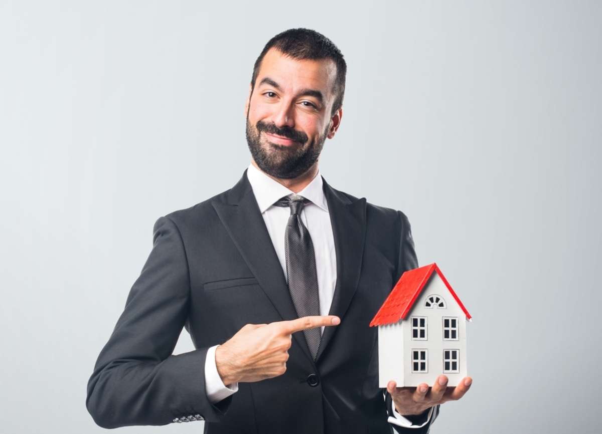 Businessman holding a little house over grey background