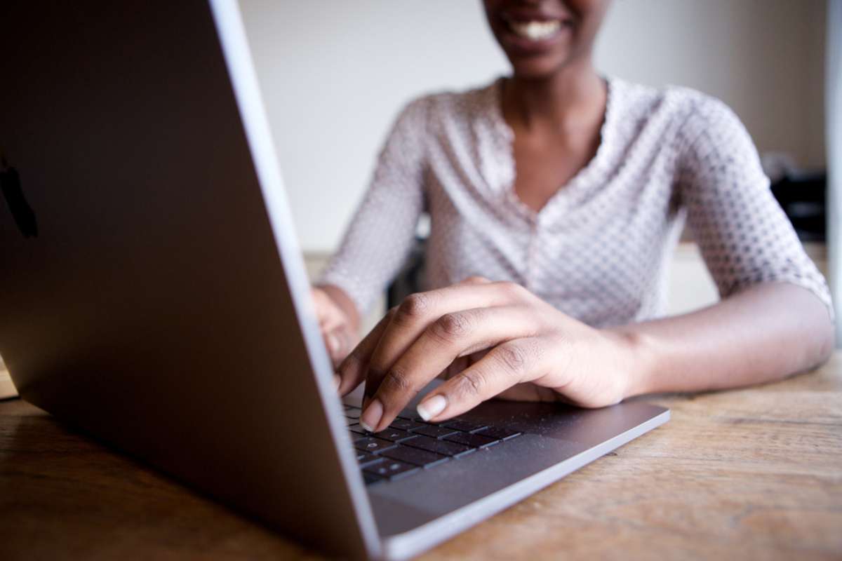 Close up partial portrait of smiling woman sitting at desk and typing on laptop computer