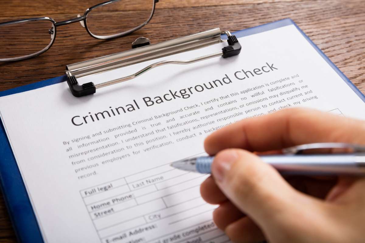 Close-up Of Person Hand Filling Criminal Background Check Application Form