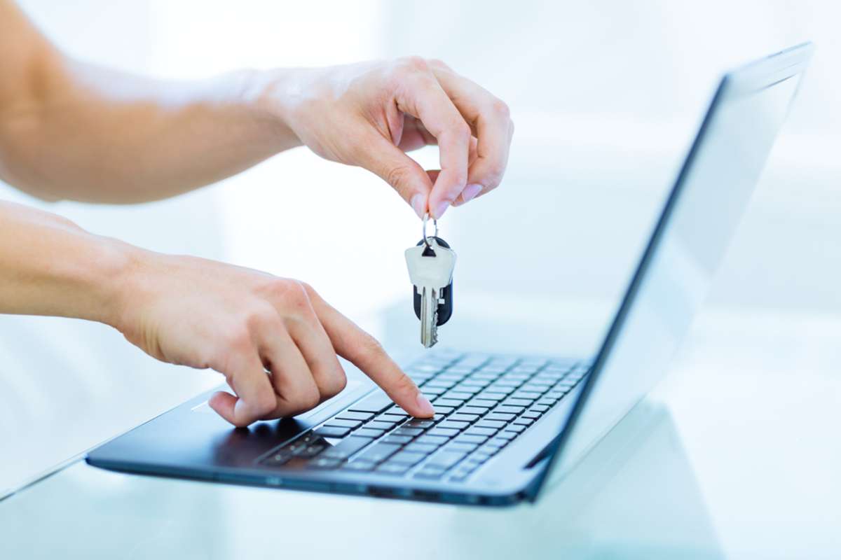 Close-up of male persons hands holding up keys while typing on a laptop computer keyboard