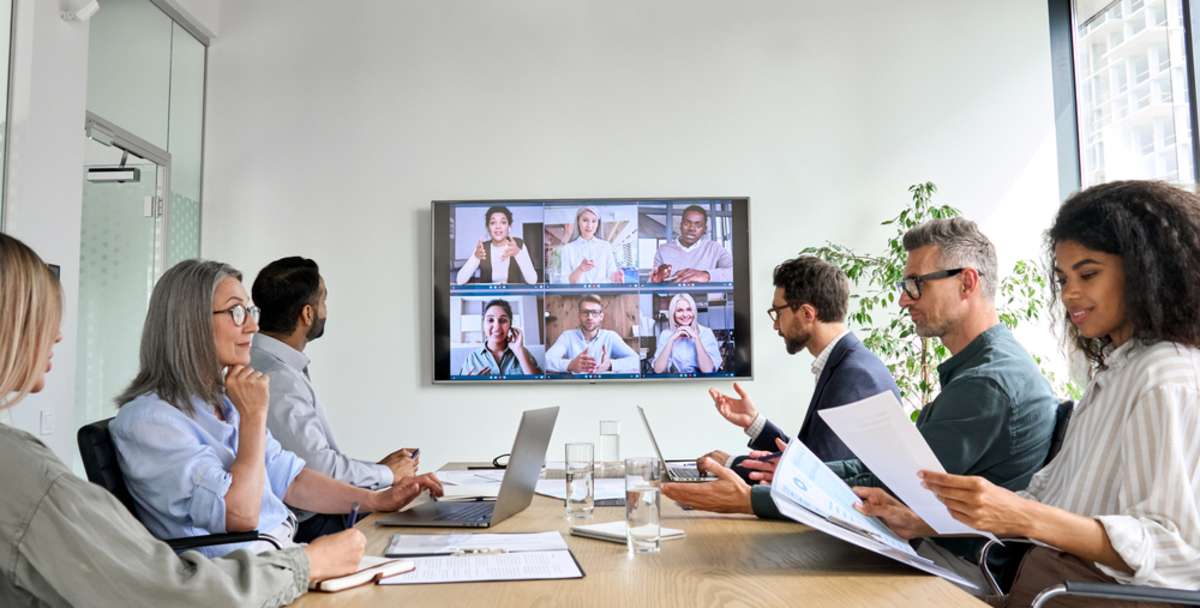 Diverse company employees having online business conference video call on tv screen monitor in board meeting room