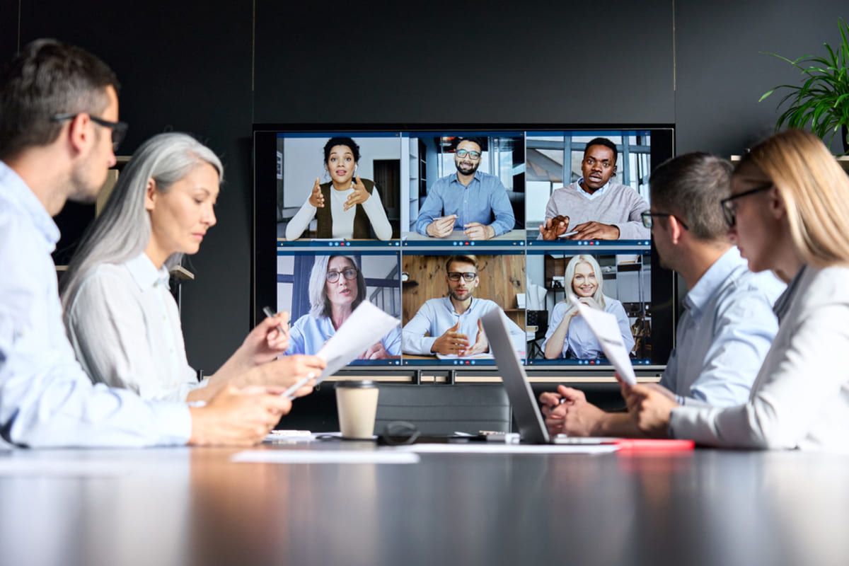 Employees meet in a conference room with a virtual team on screen, property management virtual assistant concept