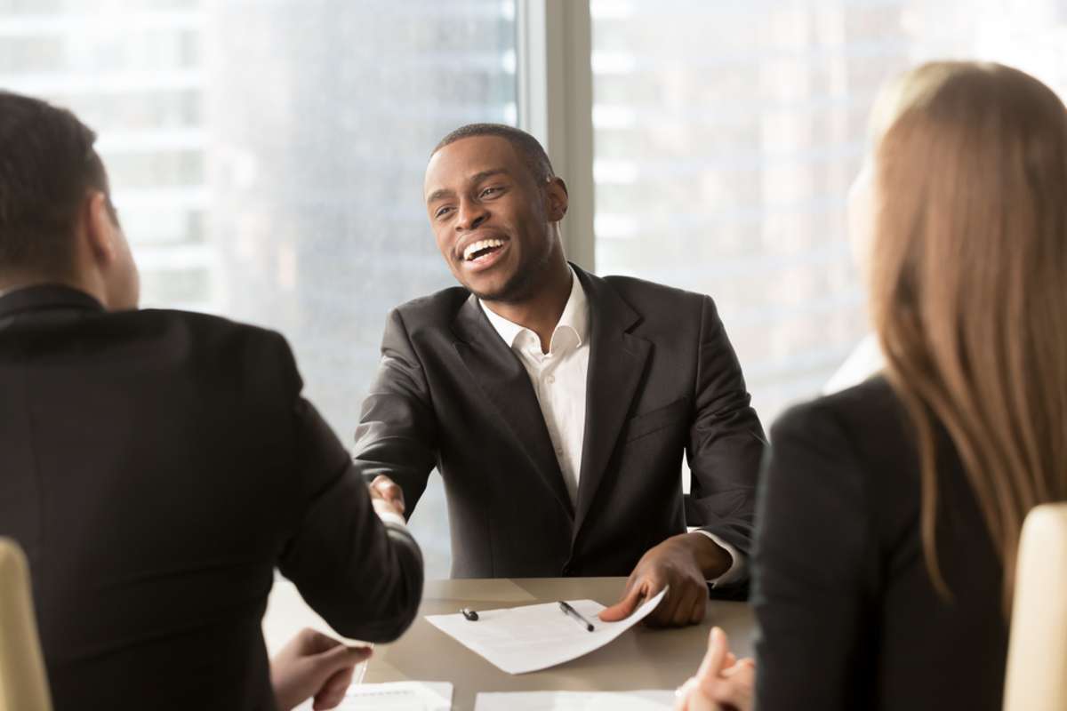 Excited smiling black businessman handshaking white partner at meeting