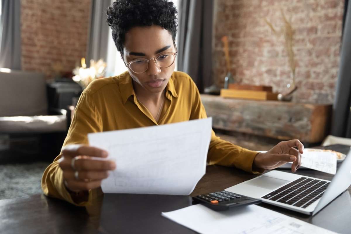 Focused young African American woman in eyeglasses looking through paper documents