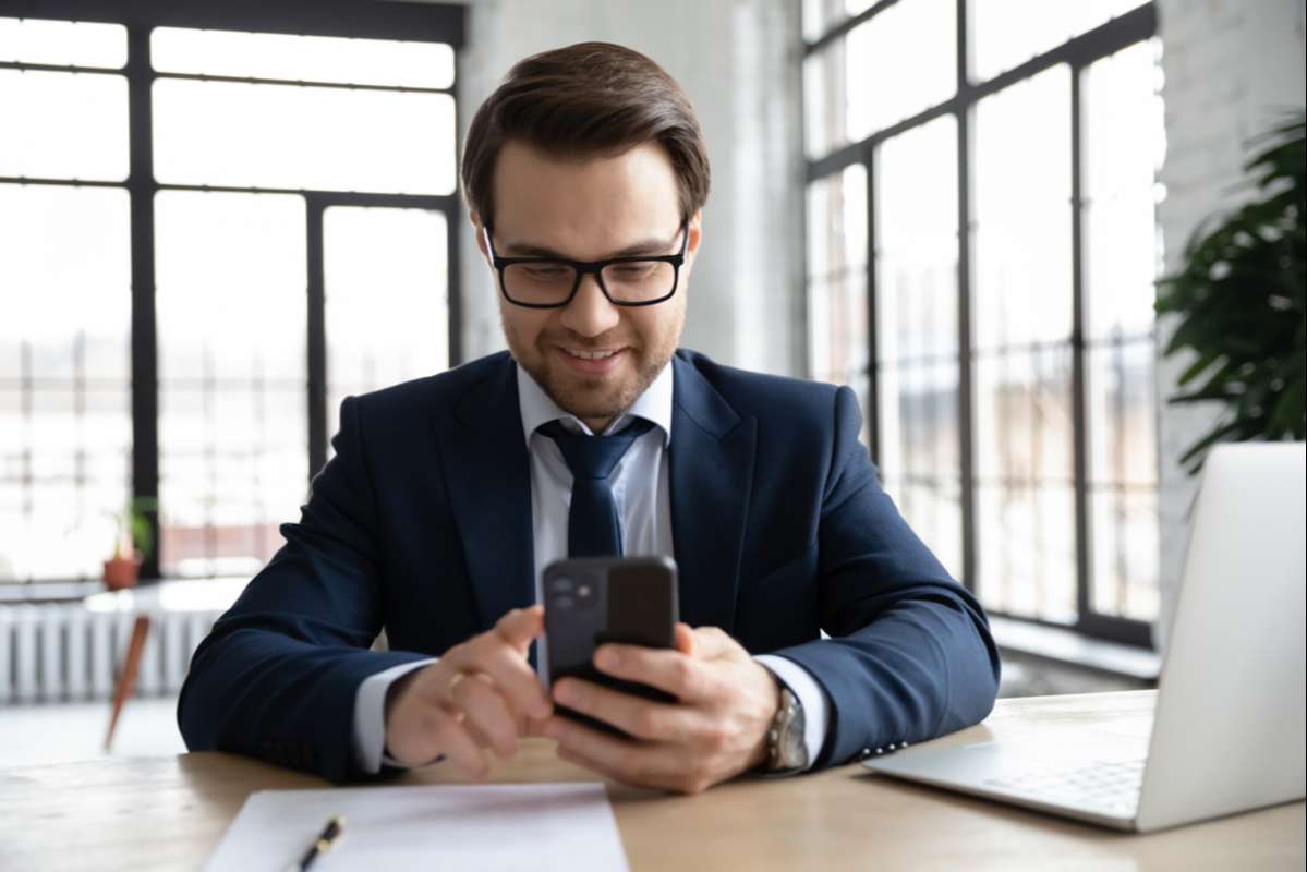Happy businessman using online app on smartphone at office workplace