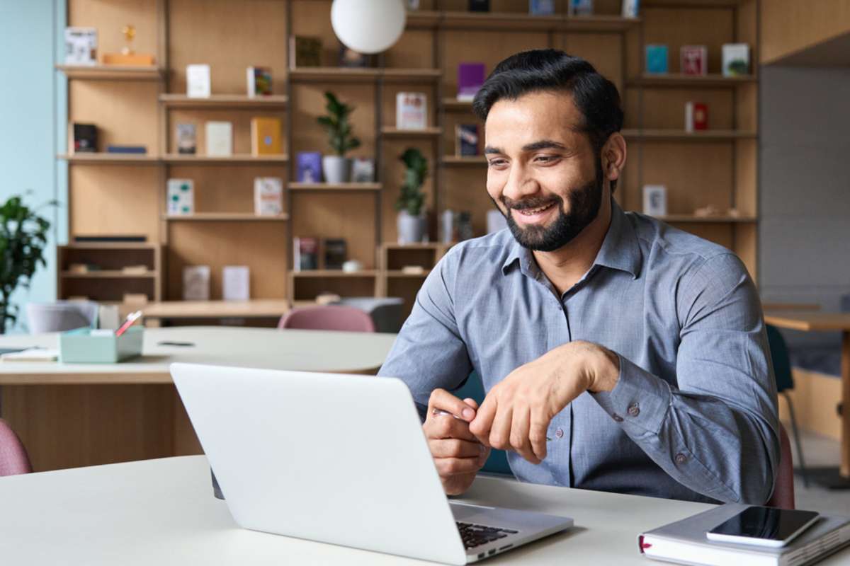 Happy smiling man working on laptop as a property management virtual assistant.