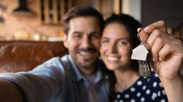 Happy young husband and wife showing key at camera, taking selfie. Property buyers, tenants celebrating mortgage approval, rent apartment, buying first house