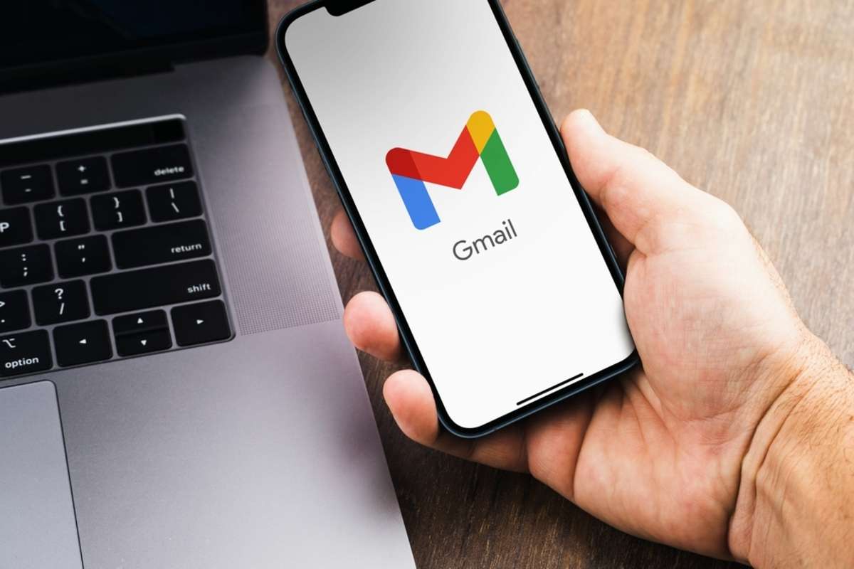 Male hand holding a smartphone with Gmail app on the screen with a computer beside it