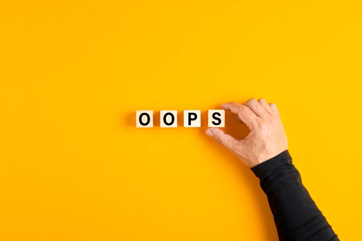 Male hand placing the wooden cubes with the word oops on yellow background