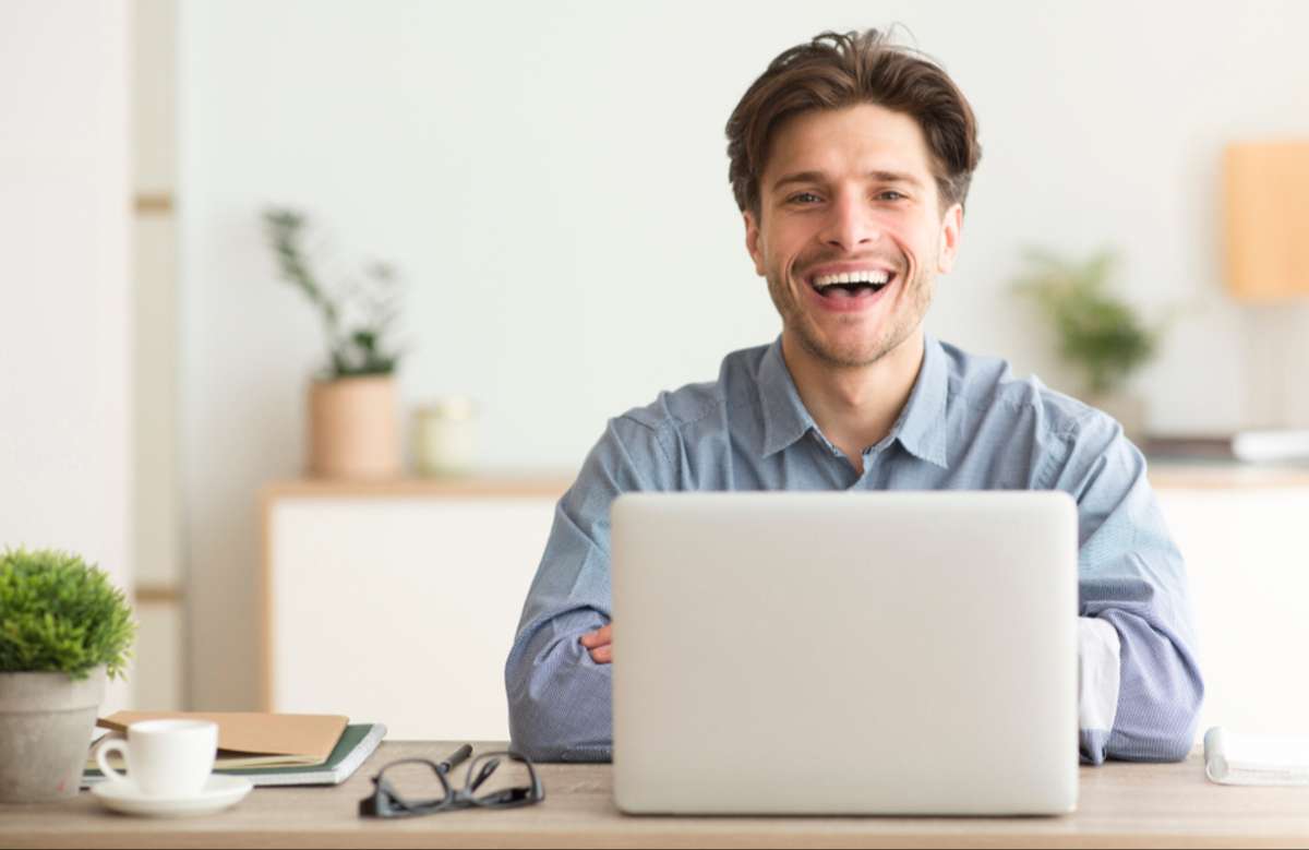 Man Sitting At Laptop And Laughing Looking At Camera Indoor