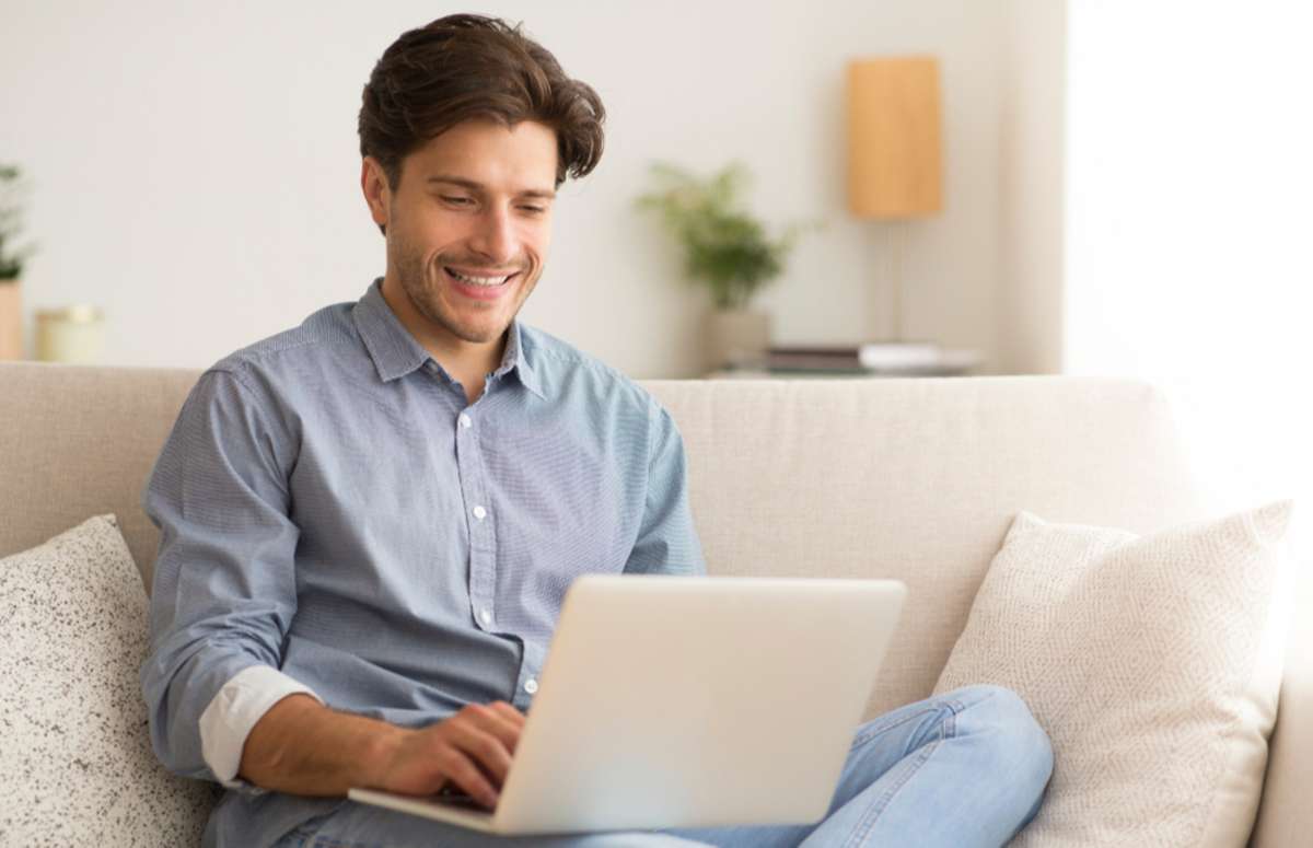 Man Working On Laptop Sitting On Sofa At Home