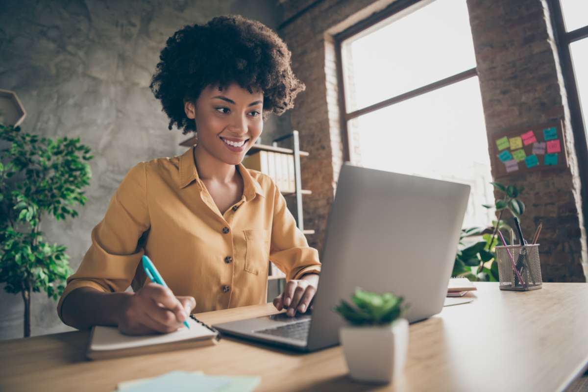 Photo of cheerful joyful mixed-race woman in yellow shirt smiling toothily writing down notes holding training for students to be executives at laptop desktop table