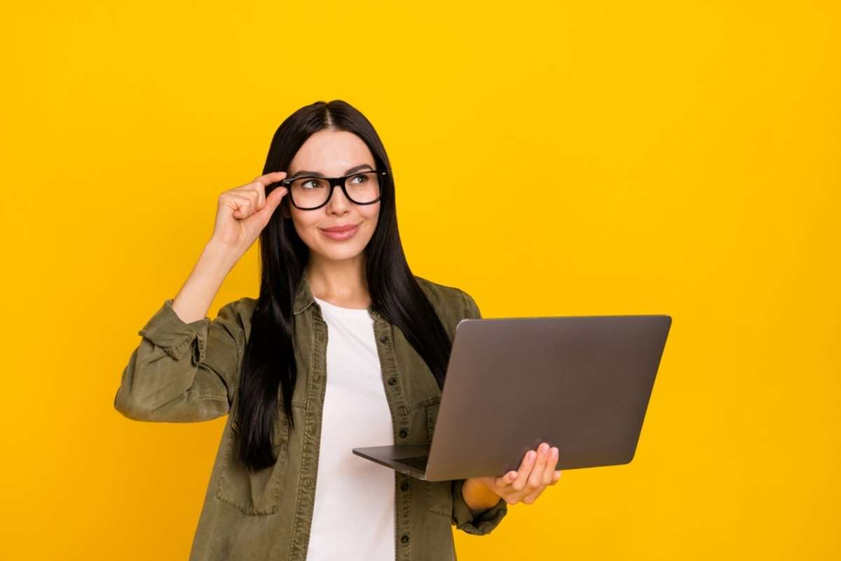 Photo of pretty young lady hold laptop look ad wear eyewear khaki shirt isolated on yellow background