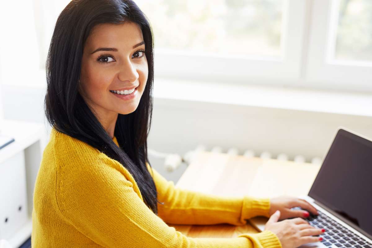 Portrait of smiling woman sitting at her desk working with laptop in the home office