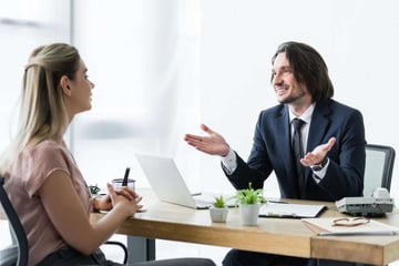 A man talks to a woman at a desk about building a virtual team. 