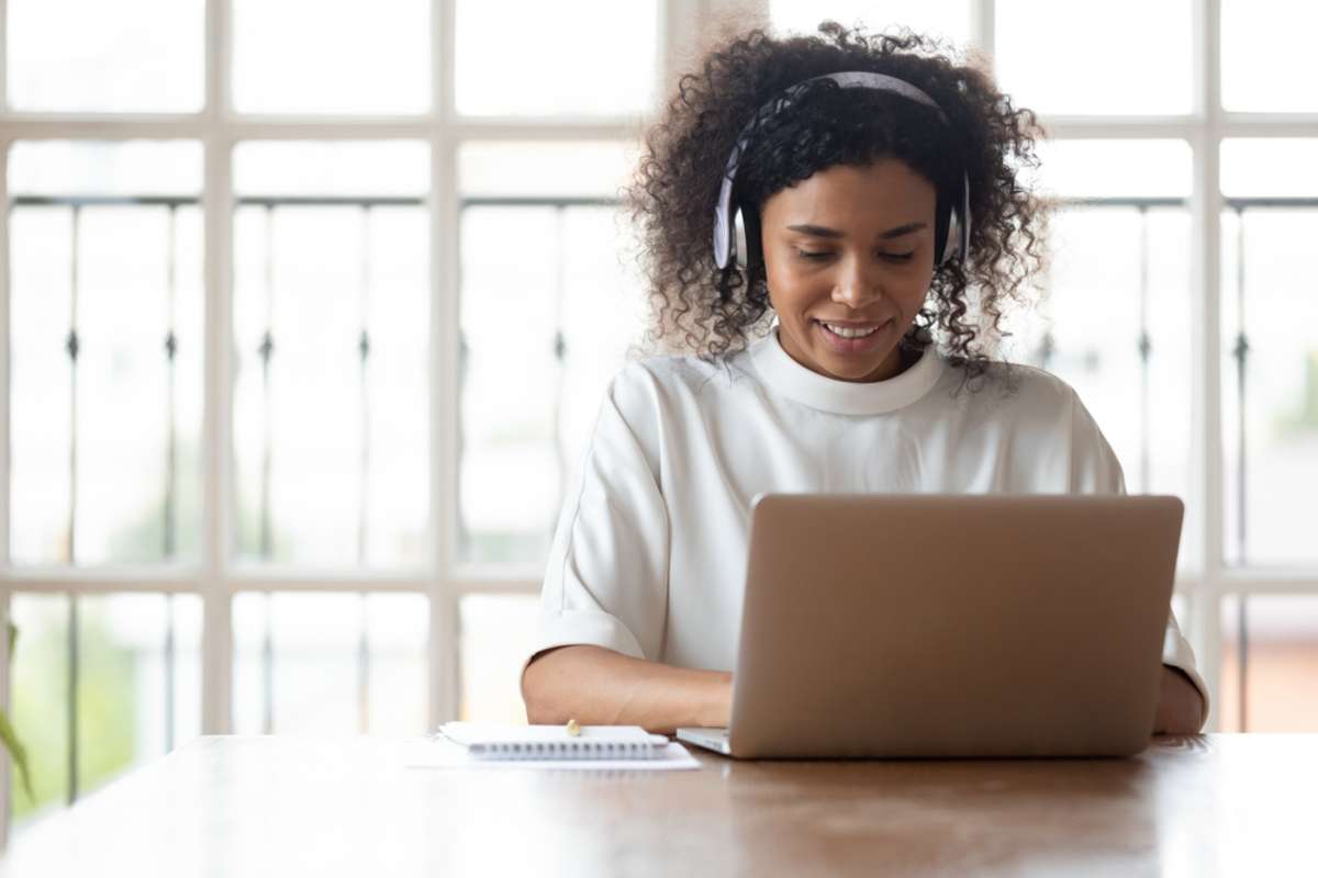 Smiling African ethnicity businesswoman wearing headphones using laptop at work