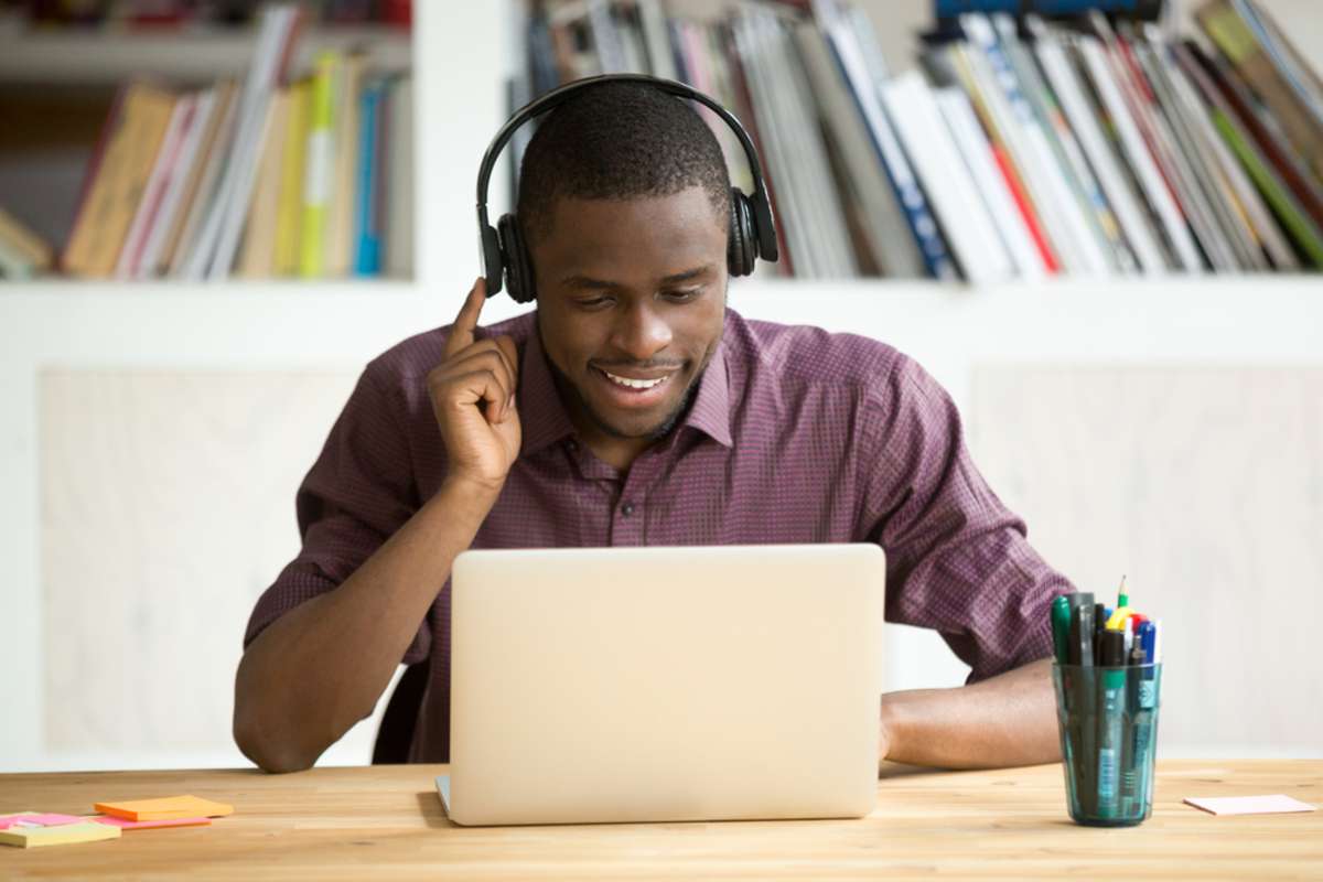 Smiling african american office worker in headphones looking at laptop screen