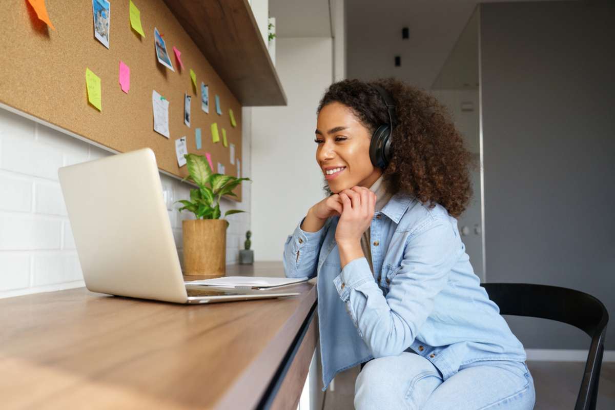 Smiling young girl wears headphones to watch video on laptop, virtual assistant training concept. 