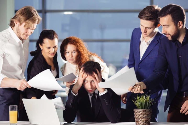 Stressed Business Man In Office surrounded by colleagues with documents in hands