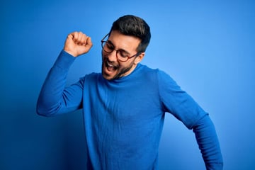 Young handsome man with beard wearing casual sweater and glasses over blue background Dancing happy and cheerful