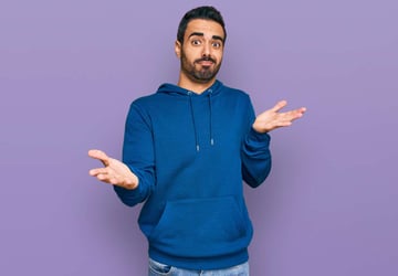 Young hispanic man wearing casual clothes clueless and confused expression with arms and hands raised