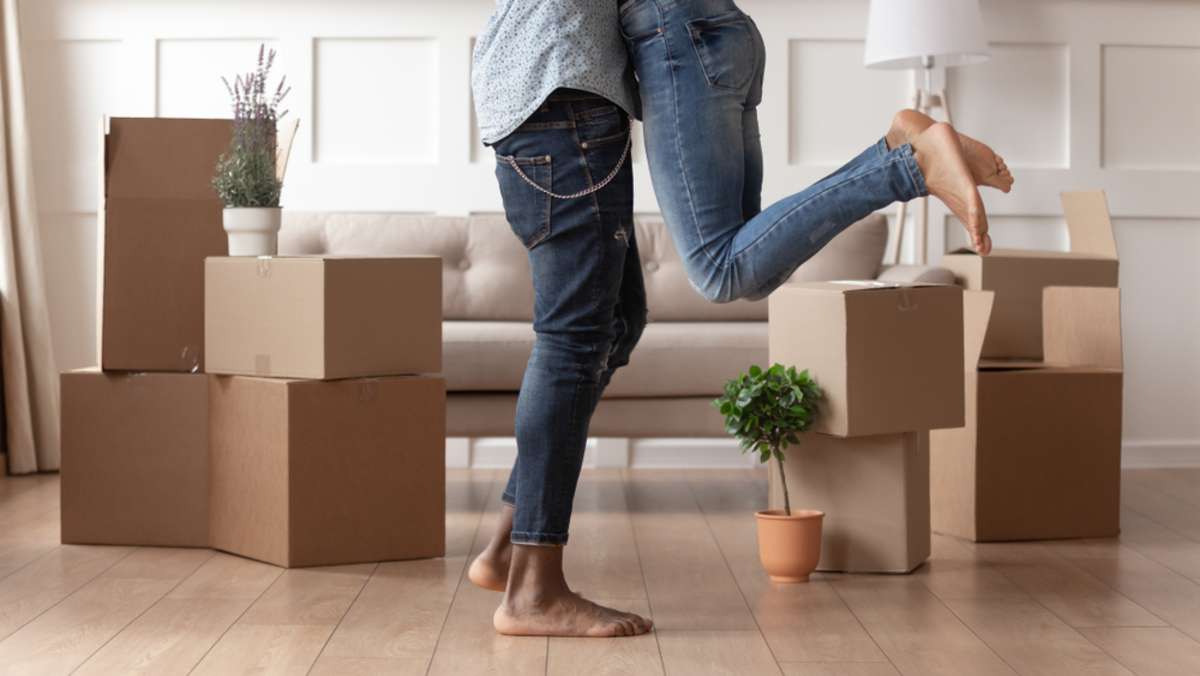 happy couple tenants homeowners on moving day in the living room with cardboard boxes, man and woman in first own apartment, mortgage or rent
