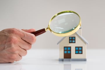 Hand with magnifying glass over house model.