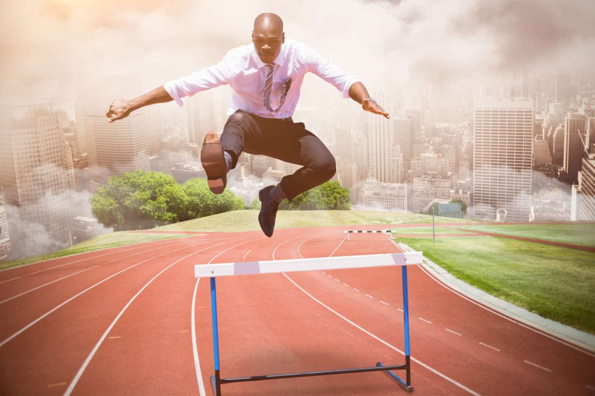 Businessman jumping a hurdle against composite image of racetrack in city