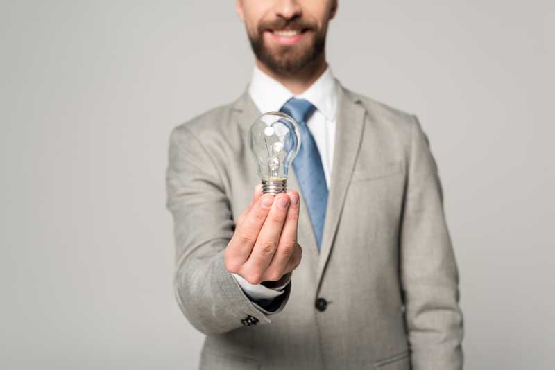 A smiling businessman holding light bulb, managing a property management virtual assistant properly. 