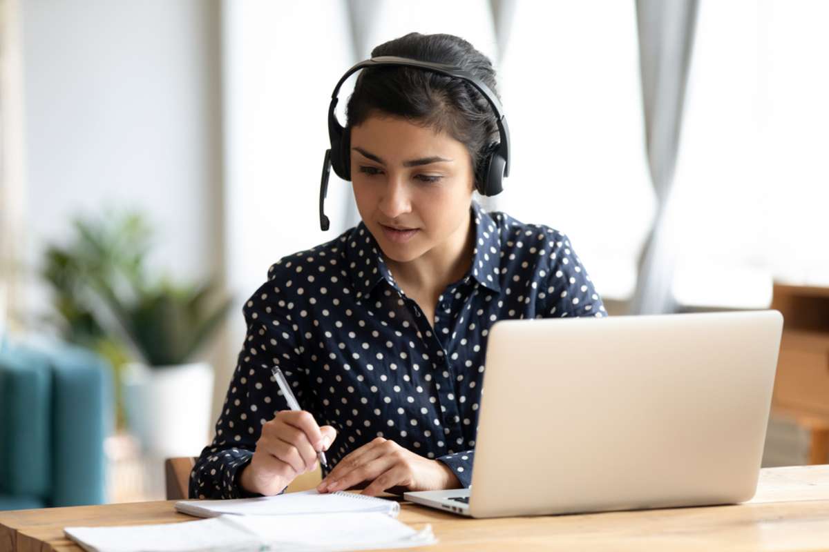 Focused Indian girl wearing headset writing notes in notebook