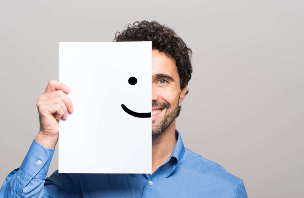 Happy man covering half his face with a smiling emoticon as finds a remote team member.