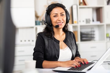 A woman with a headset working at a computer. 