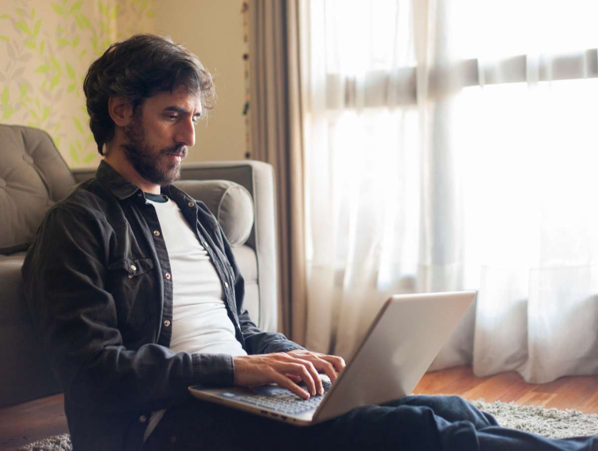 Man working on a laptop in living room, remote team members concept. 