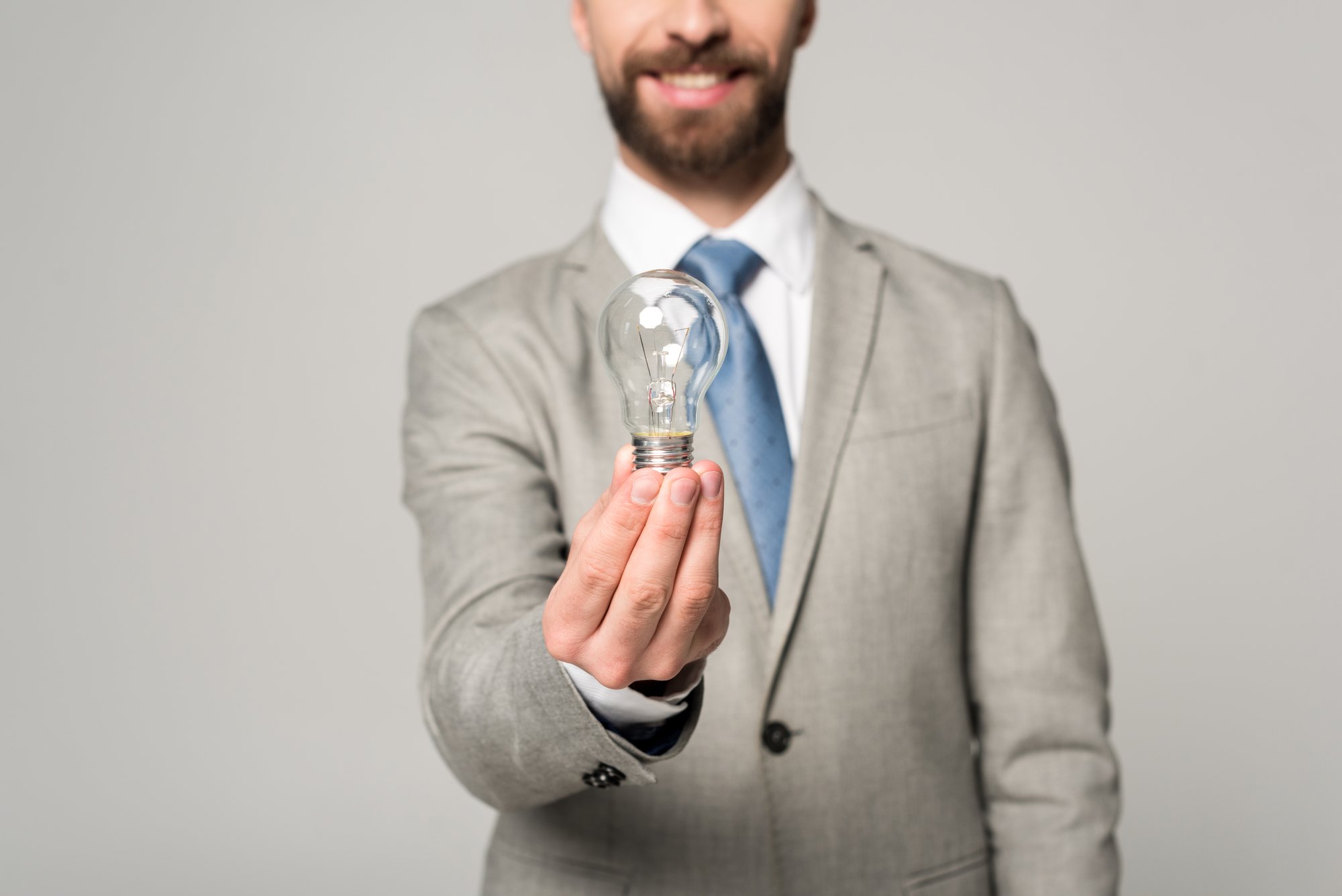 Partial view of smiling businessman holding light bulb isolated on grey