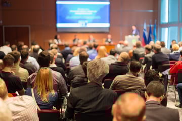 Rear view of an audience watching a panel at a conference.