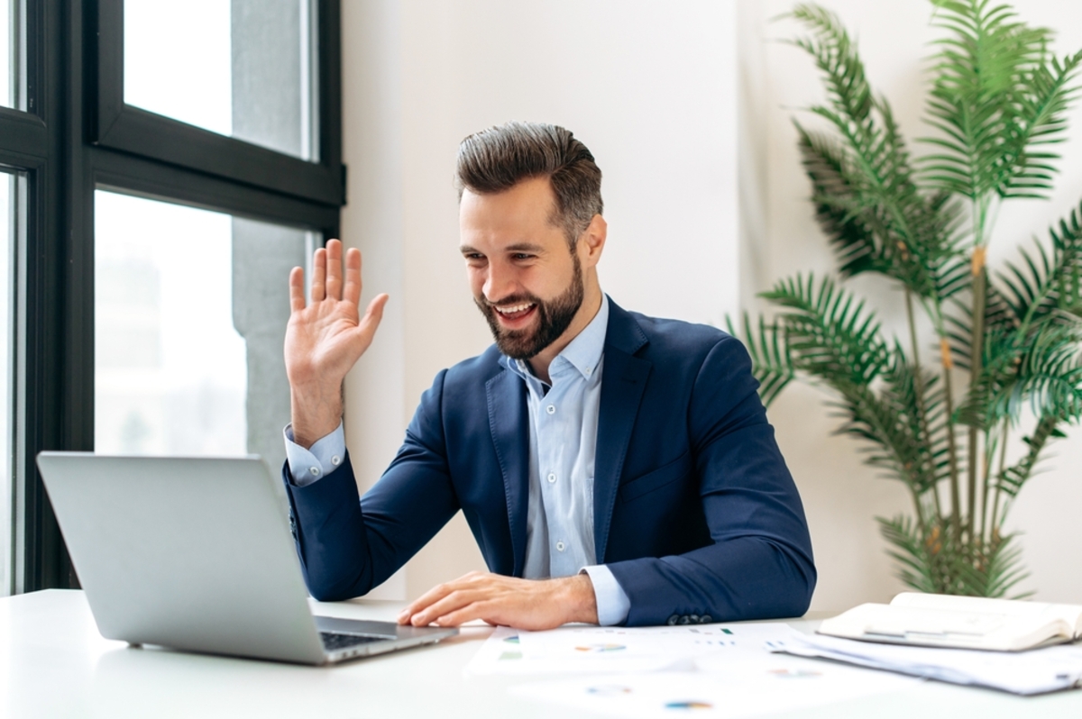 A man waving and recording on his laptop