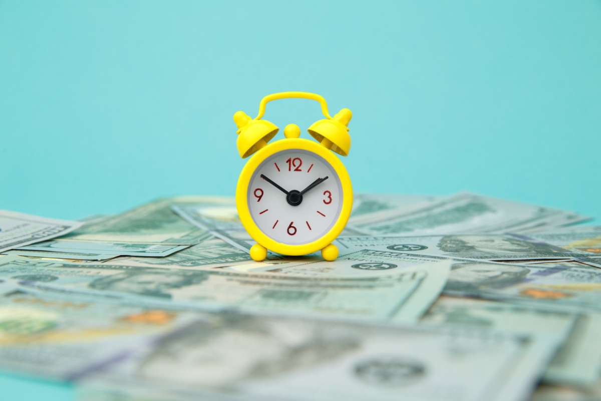 Close-up of yellow alarm clock and money on blue background