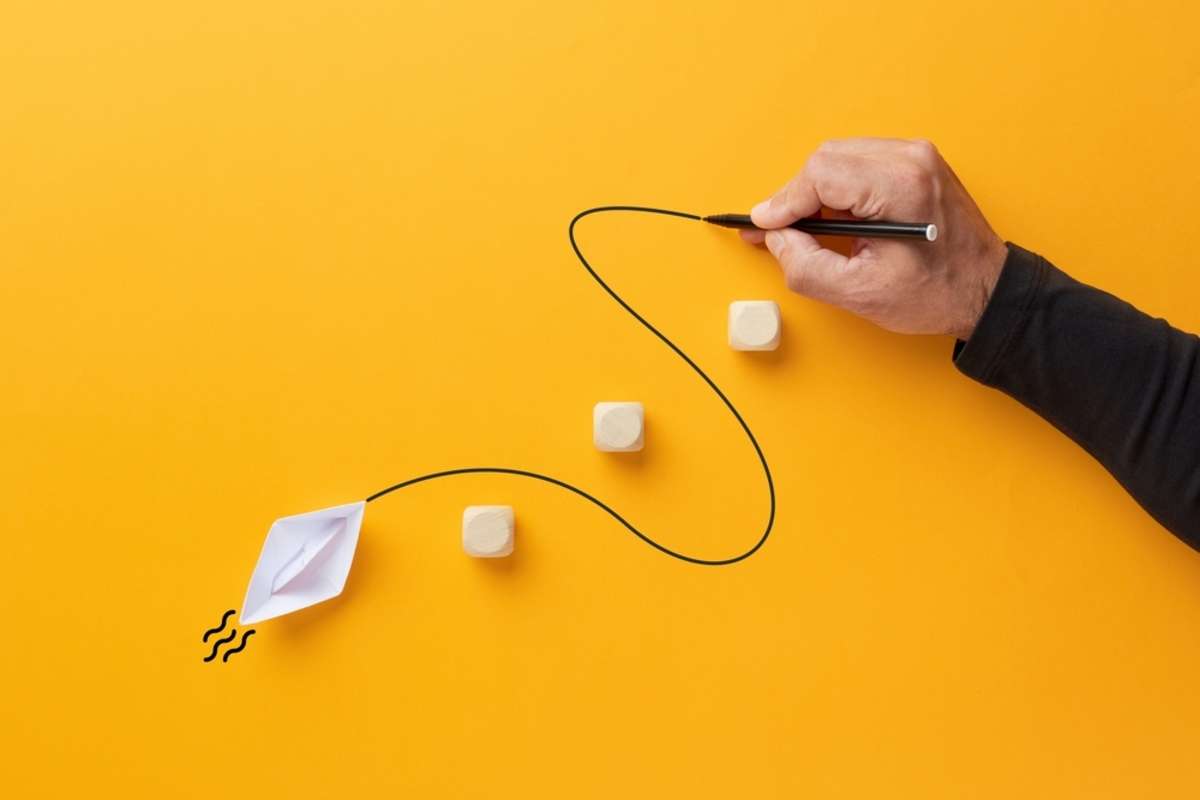 Male hand draws a curved line that guides a paper boat to cross the barriers